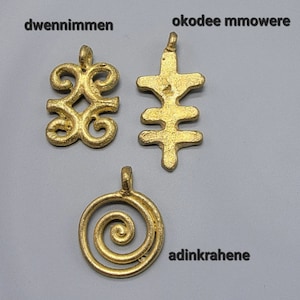 May include: Three gold-colored pendants with different designs. The first pendant is a stylized symbol called "dwennimmen". The second pendant is a stylized symbol called "okodee mmowere". The third pendant is a stylized symbol called "adinkrahene".