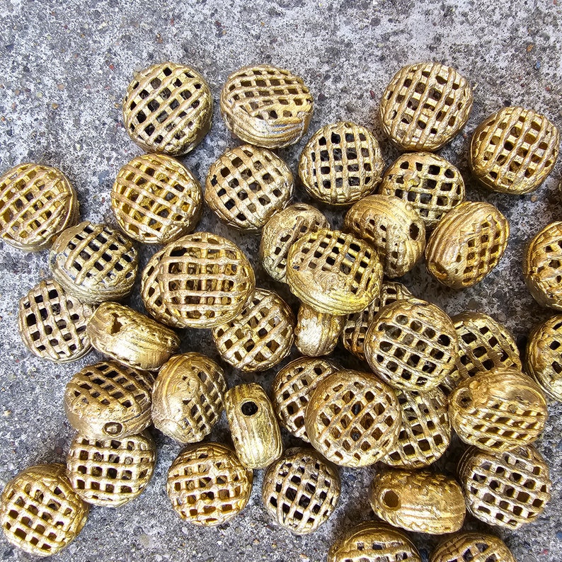 May include: A collection of gold-colored metal beads with a lattice design. The beads are round and have a slightly irregular shape.