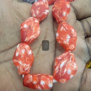 May include: A strand of orange and white marbled beads. The beads are irregularly shaped and strung together. The number "5" is visible in a gray box. The beads are a vibrant orange color with white marbling throughout.