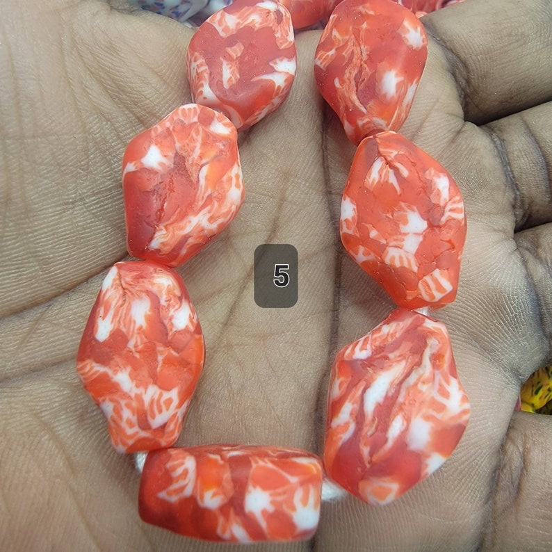 May include: A strand of orange and white marbled beads. The beads are irregularly shaped and strung together. The number "5" is visible in a gray box. The beads are a vibrant orange color with white marbling throughout.