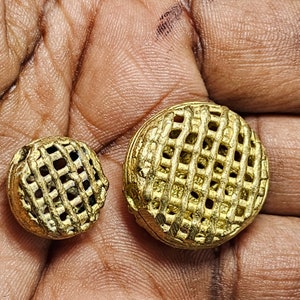 May include: Two gold-colored metal buttons with a grid pattern. The buttons are round and have a raised design.