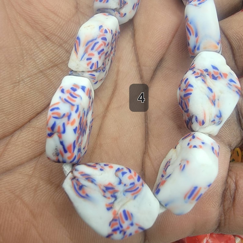 May include: A strand of white beads with a speckled pattern of blue and orange dashes. The beads are irregularly shaped and strung together. The number "4" is in a square in the background.