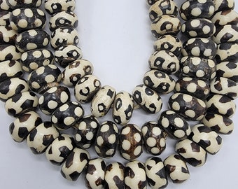 May include: A close-up of a necklace made of white and black patterned beads. The beads are round and have a smooth, polished finish. The necklace is made of multiple strands of beads, and the beads are arranged in a random pattern.