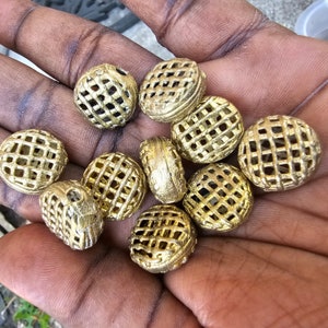 May include: A collection of 10 gold-colored metal beads with a grid pattern. The beads are round and have a slightly textured surface.