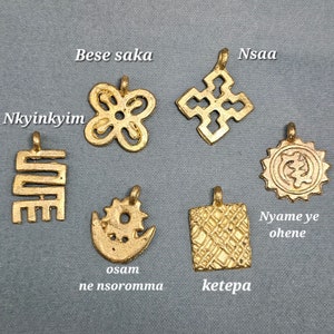 May include: Seven gold-colored pendants with different designs and symbols. The pendants are labeled with the words "Nkyinkyim", "Bese saka", "Nsaa", "Osam ne nsoromma", "Ketepa", and "Nyame ye ohene".