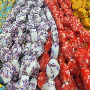 May include: Close-up of colorful beads in various colors. White beads with red and blue streaks, red beads with white swirls, and yellow beads are visible. The beads are strung together, creating a vibrant display of colors and patterns.