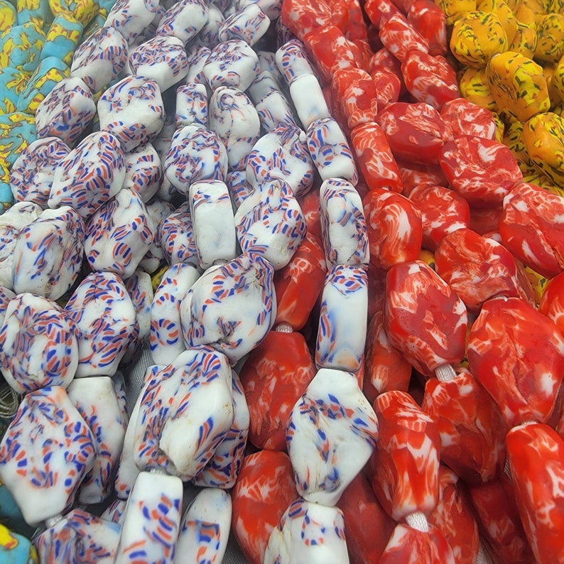 May include: Close-up of colorful beads in various colors. White beads with red and blue streaks, red beads with white swirls, and yellow beads are visible. The beads are strung together, creating a vibrant display of colors and patterns.