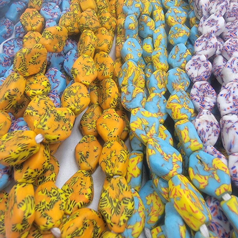 May include: Close-up of colorful beads in shades of orange, yellow, blue, and white. The beads have unique patterns and shapes, strung together on white string. The beads are likely for jewelry making or craft projects.