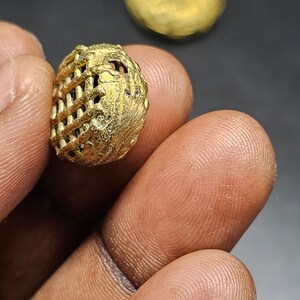 May include: A gold-colored metal bead with a geometric, lattice-like design. The bead has a small hole in the center.