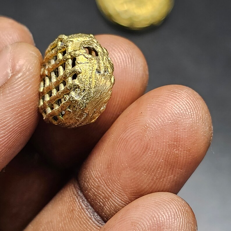 May include: A gold-colored metal bead with a geometric, lattice-like design. The bead has a small hole in the center.