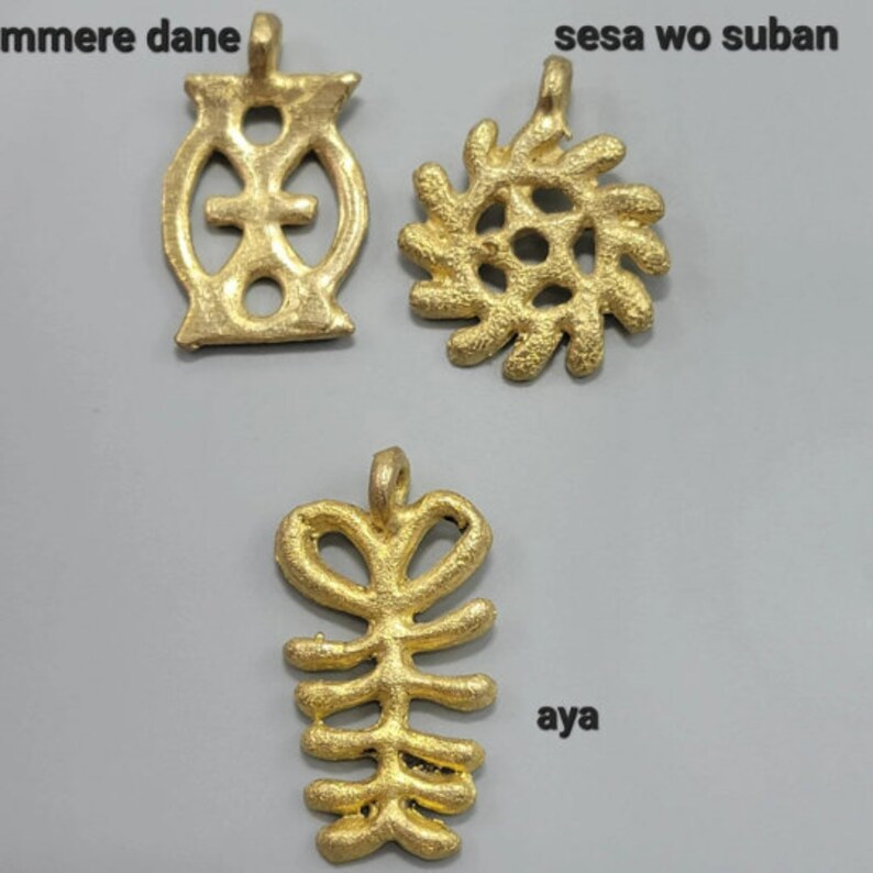 May include: Three gold-colored metal pendants with intricate designs. The pendant on the left is a circle with a cross inside. The pendant in the middle is a spiral design. The pendant on the right is a more abstract design with a series of lines and curves.