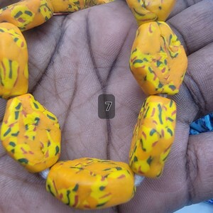 May include: Close-up of a strand of chunky, irregular beads. The beads are a vibrant yellow-orange color with a speckled pattern of red, green, and yellow. The beads are strung on a white cord. The number 7 is visible.
