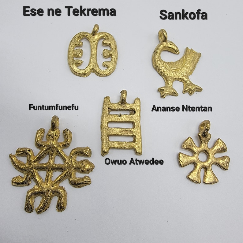 May include: Six gold-colored metal pendants with different designs and names in black text. The pendants are: Ese ne Tekrema, Sankofa, Funtumfunefu, Owuo Atwedee, Ananse Ntentan, and a star-shaped pendant.