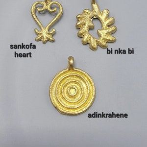 May include: Three gold-colored Adinkra symbols, each with a different design. The symbols are called "sankofa heart", "bi nka bi", and "adinkrahene".