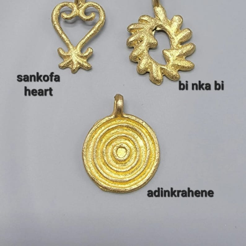 May include: Three gold-colored Adinkra symbols, each with a different design. The symbols are called "sankofa heart", "bi nka bi", and "adinkrahene".