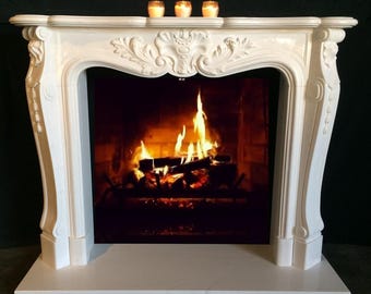 Puede incluir: Una repisa de chimenea blanca con tallas ornamentadas y una abertura rectangular. La chimenea presenta un fuego encendido y tres velas encendidas en la repisa. El diseño es clásico y elegante.