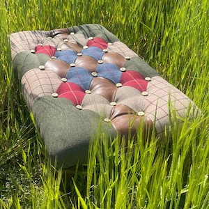 May include: A rectangular ottoman with a patchwork design. The top features sections of brown leather, red and blue plaid, and green and brown tweed fabrics. The ottoman is button-tufted and has wooden legs.