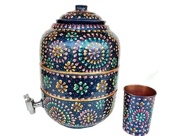 Könnte beinhalten: Ein handbemalter, dunkelblauer Wasserspender mit passendem Deckel und Auslaufhahn. Der Spender und der dazugehörige Becher sind mit bunten Blumenmustern verziert. Die Innenseite des Bechers ist kupferfarben.