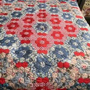 May include: A red, white and blue patchwork quilt with a hexagonal pattern. The quilt is made of various fabrics and has a vintage look.