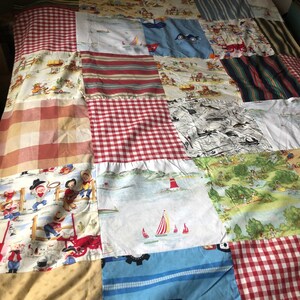 May include: A patchwork quilt featuring a range of colourful patterns, including red and white gingham, blue and white stripes, and a nautical theme. The quilt is made up of numerous squares, each with a distinct design.