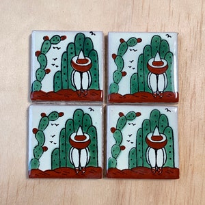 Puede incluir: Conjunto de cuatro azulejos de cerámica con un diseño tradicional de arte popular mexicano. Cada azulejo representa a una persona con un sombrero y de pie frente a un cactus. Los azulejos están pintados en tonos de verde, marrón, blanco y rojo.