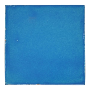 Könnte beinhalten: Eine quadratische Keramikfliese in einem kräftigen, leuchtenden Blau. Die Fliese hat eine leicht strukturierte Oberfläche und eine glänzende Oberfläche. Die Kanten weisen leichte Abnutzungserscheinungen auf, was darauf hindeutet, dass sie möglicherweise vintage oder handgefertigt ist. Diese Fliese kann für Heimdekoration oder Bastelprojekte verwendet werden.