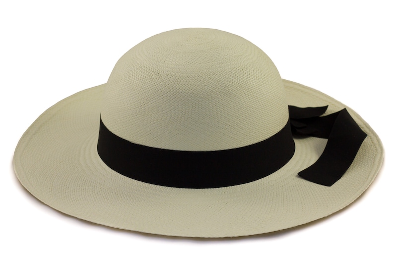 Pu&ograve; includere: Un cappello Panama beige chiaro con un'ampia tesa e un nastro nero attorno alla corona. Il nastro ha un fiocco su un lato.