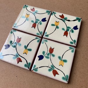 May include: Four square ceramic tiles with a white background and a floral design. The design features black outlines of stems with red, yellow, and blue flowers.