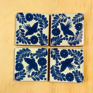 May include: Four square ceramic tiles with a white background and blue floral designs. Each tile features a stylised bird with a floral pattern surrounding it.