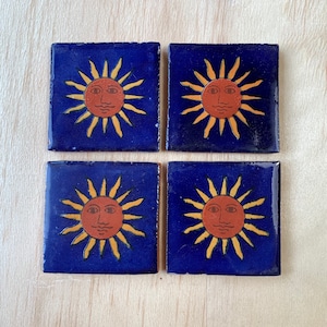 Könnte beinhalten: Set aus vier blauen Keramik-Untersetzern mit einem gelben Sonnenmotiv mit rotem Gesicht.