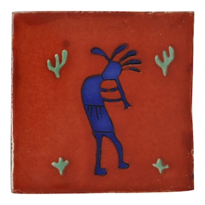 Könnte beinhalten: Quadratische Keramikfliese mit rotem Hintergrund und einer blauen Kokopelli-Figur, die Flöte spielt. Die Fliese hat grüne Kaktus- und sternförmige Akzente. Die Fliese ist quadratisch.