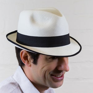 May include: A white Panama hat with a black band. The hat has a wide brim and a slightly rounded crown.