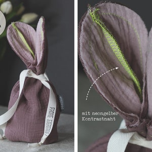 Puede incluir: Bolsa de conejo de tela malva con costuras de color amarillo ne&oacute;n y el texto "Frohe Ostern" en el lateral.