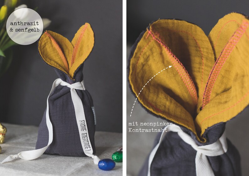 Puede incluir: Una bolsa de regalo de tela gris con un dise&ntilde;o de orejas de conejo de color amarillo mostaza. La bolsa est&aacute; atada con una cinta blanca y tiene el texto "Frohe Ostern!" impreso en el lateral.