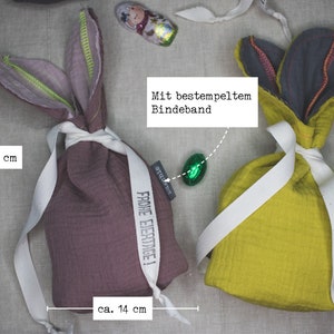 Puede incluir: Dos bolsas de regalo de Pascua de conejo de tela con una cinta blanca y el texto "Frohe Eiertage!" impreso en cada una. Las bolsas miden 14 cm de ancho y 23 cm de alto.