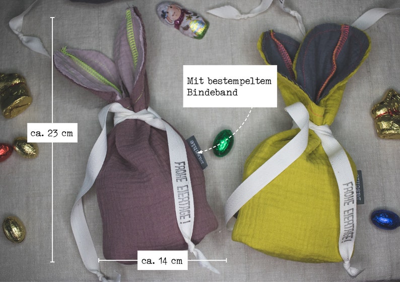 Puede incluir: Dos bolsas de regalo de Pascua de conejo de tela con una cinta blanca y el texto "Frohe Eiertage!" impreso en cada una. Las bolsas miden 14 cm de ancho y 23 cm de alto.