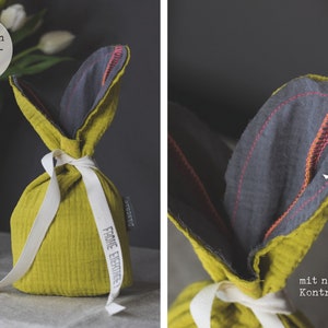 Puede incluir: Una bolsa de Pascua de conejo de tela verde con forro de tela gris y una cinta blanca. La bolsa tiene el texto "From Evertree" impreso en ella. La bolsa est&aacute; atada con una cinta blanca y tiene una puntada de contraste rosa ne&oacute;n.