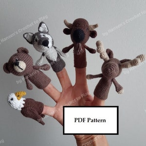 May include: A set of five finger puppets featuring a bear, wolf, bison, moose, and eagle. The puppets are crocheted in brown, white, and grey yarn. The puppets are on a hand, with the text "PDF Pattern" visible in the lower right corner.