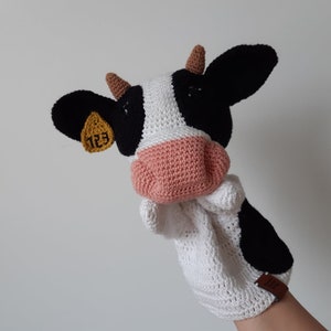 May include: A white and black crocheted cow puppet with a pink nose and a yellow tag with the number 123 on it.