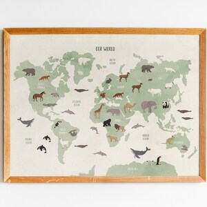 K&ouml;nnte beinhalten: Eine gerahmte Weltkarte mit einem gr&uuml;nen und beigen Farbschema. Die Karte zeigt Illustrationen von Tieren, die auf verschiedenen Kontinenten beheimatet sind, darunter ein Eisb&auml;r, eine Giraffe, ein K&auml;nguru und ein Pinguin. Der Text "OUR WORLD" ist oben auf der Karte gedruckt.