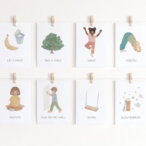 May include: Eight illustrated cards with different activities for kids. The cards are hung on a white wall with wooden clothespins. The activities include eating a snack, taking a walk, dancing, stretching, meditating, pushing on the wall, swinging, and blowing bubbles.