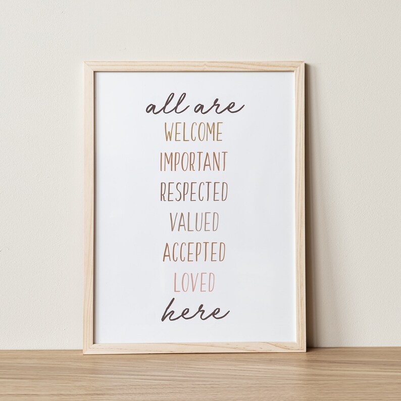 May include: A framed print with the text "all are welcome important respected valued accepted loved here" in a light brown wood frame.