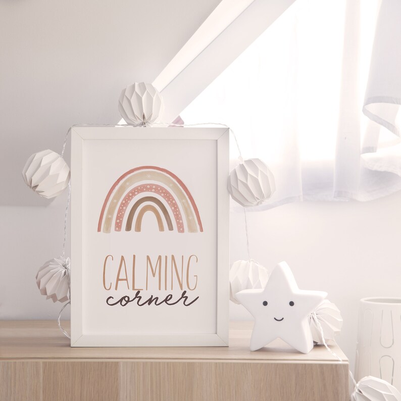 Puede incluir: Una impresi&oacute;n enmarcada en blanco con un arco&iacute;ris de acuarela en tonos rosa, marr&oacute;n y naranja con lunares blancos. El texto "CALMING corner" est&aacute; escrito en marr&oacute;n debajo del arco&iacute;ris.