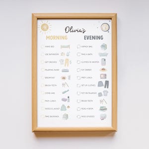 May include: A framed daily routine chart with the name "Olivia's" at the top. The chart is divided into "Morning" and "Evening" sections, each with illustrated tasks like "Make Bed," "Brush Teeth," and "Read a Book." The frame is made of light brown wood.