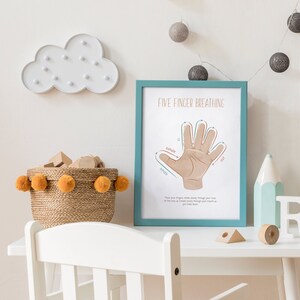 May include: A teal framed poster with the title "Five Finger Breathing" and a diagram of a hand with arrows showing how to breathe in and out. The poster is on a white table with a basket of yellow pom-poms and wooden blocks.