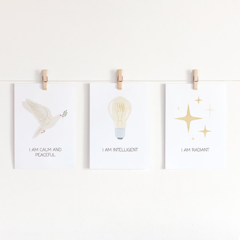 May include: Three white cards with positive affirmations and illustrations. The first card has a white dove with an olive branch in its beak and the text "I am calm and peaceful". The second card has a lightbulb and the text "I am intelligent". The third card has gold stars and the text "I am radiant".