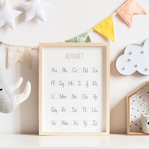 Peut inclure: Un tableau d'alphabet encadr&eacute; avec les lettres de l'alphabet &eacute;crites en minuscules. Le tableau est accroch&eacute; &agrave; un mur blanc avec une lumi&egrave;re en forme de nuage blanc, une &eacute;tag&egrave;re en bois avec une petite tasse en c&eacute;ramique blanche et un rhinoc&eacute;ros en peluche gris.