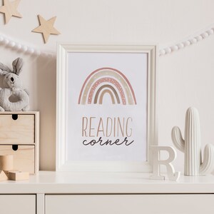 Puede incluir: Una c&oacute;moda blanca con un estampado enmarcado blanco que presenta un arco&iacute;ris con tonos marrones y rosados y el texto "READING corner". Hay un cactus blanco, una letra R de madera y un conejo de juguete de madera en la c&oacute;moda.