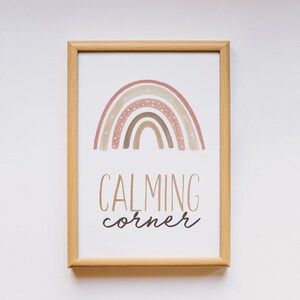 Puede incluir: Una impresi&oacute;n enmarcada con un arco&iacute;ris de acuarela en tonos rosa, marr&oacute;n y blanco sobre un fondo blanco. El texto "CALMING corner" est&aacute; impreso debajo del arco&iacute;ris.