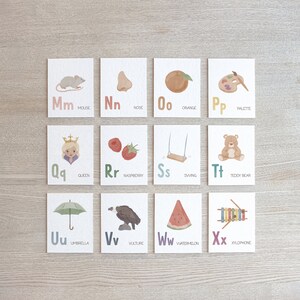 May include: A set of 26 alphabet flash cards with colorful illustrations and corresponding words. The cards feature a mouse, nose, orange, palette, queen, raspberry, swing, teddy bear, umbrella, vulture, watermelon, and xylophone.